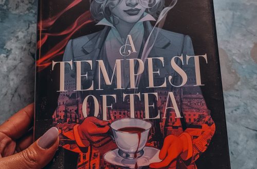 book, A Tempest of Tea, held in a brown hand with a black mug in the background
